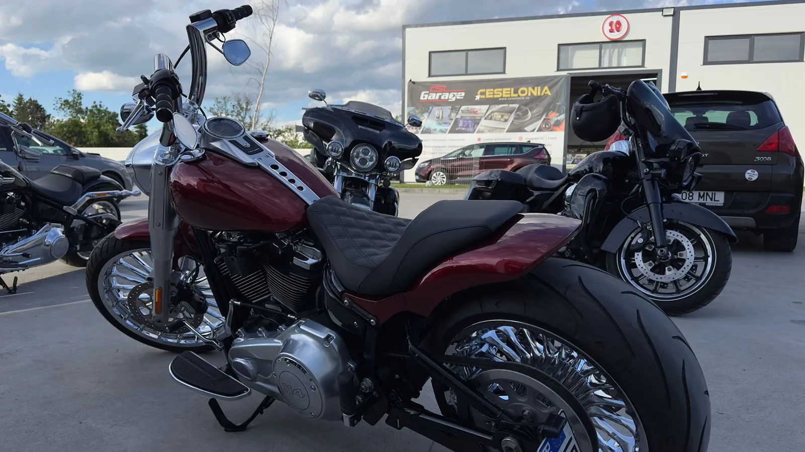 2018 Harley-Davidson Fat Boy, candy red tank and fenders with chrome spoke wheels, parked outside a garage
